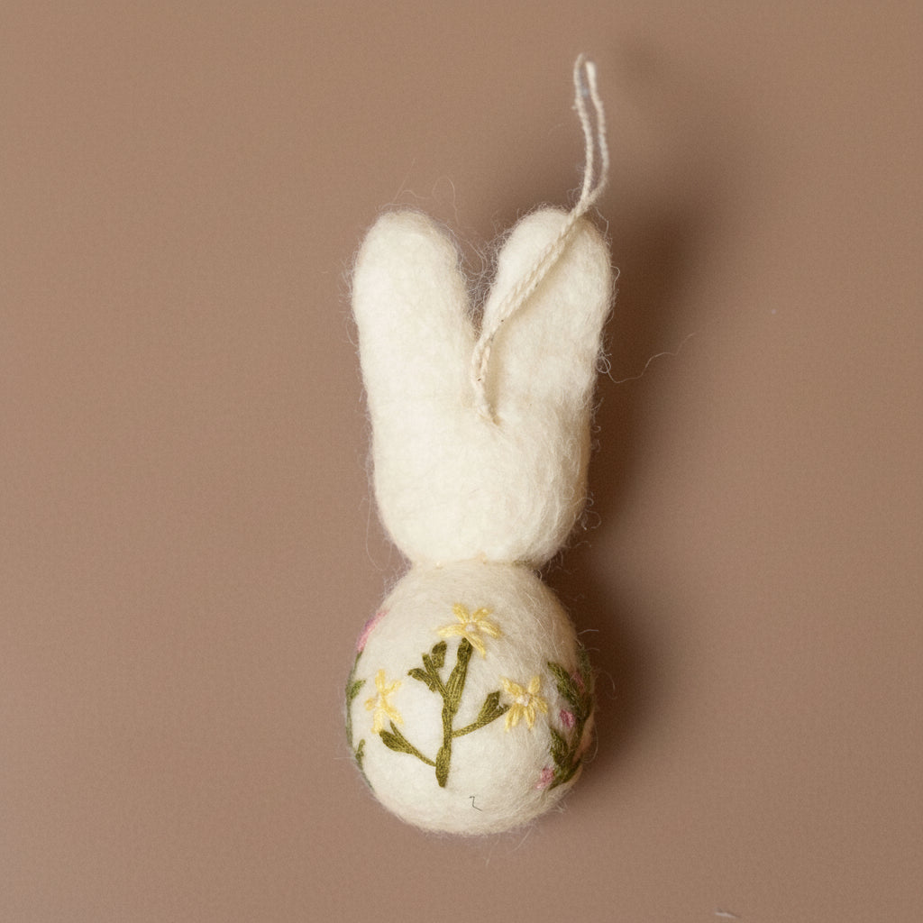 White felt bunny ornament with embroidered ball on a brown background