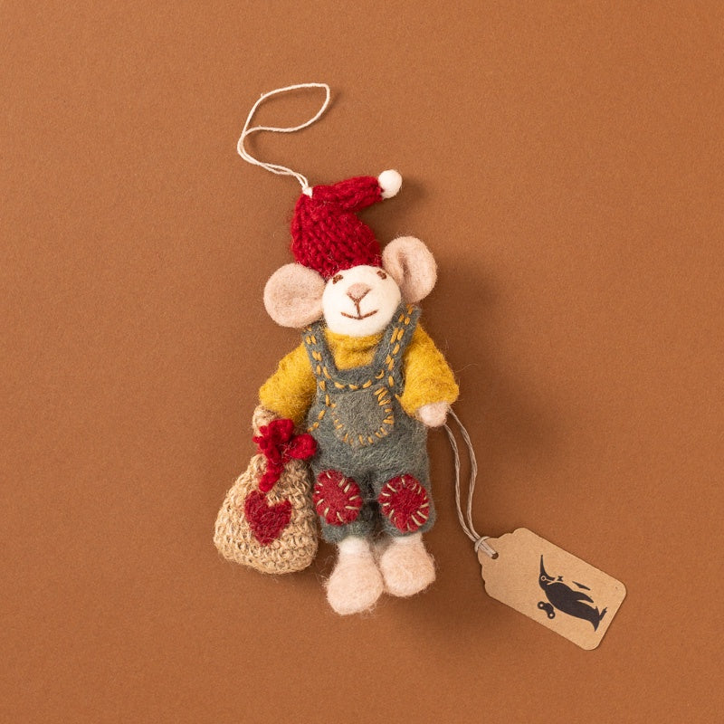 Handmade felted wool mouse ornament dressed in a red Santa hat, yellow sweater, and blue overalls, holding a small red heart-shaped bag, shown on a brown background with a hanging tag.
