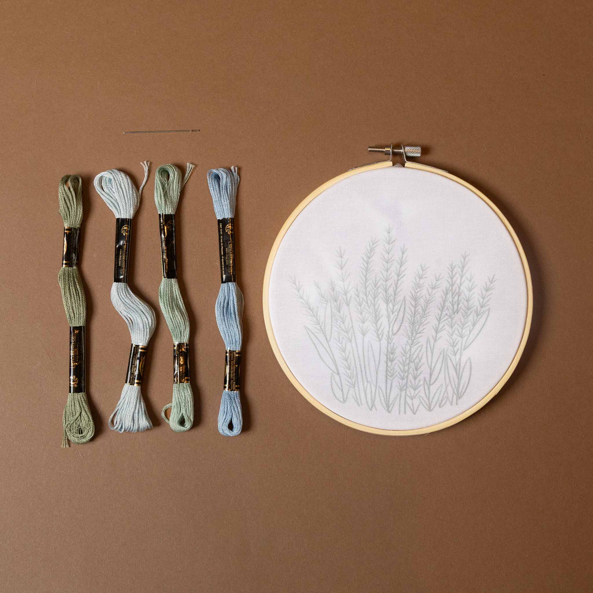 field-of-flowers-embroidery-kit-rain hoop with floral pattern and four skeins of embroidery thread on a brown background