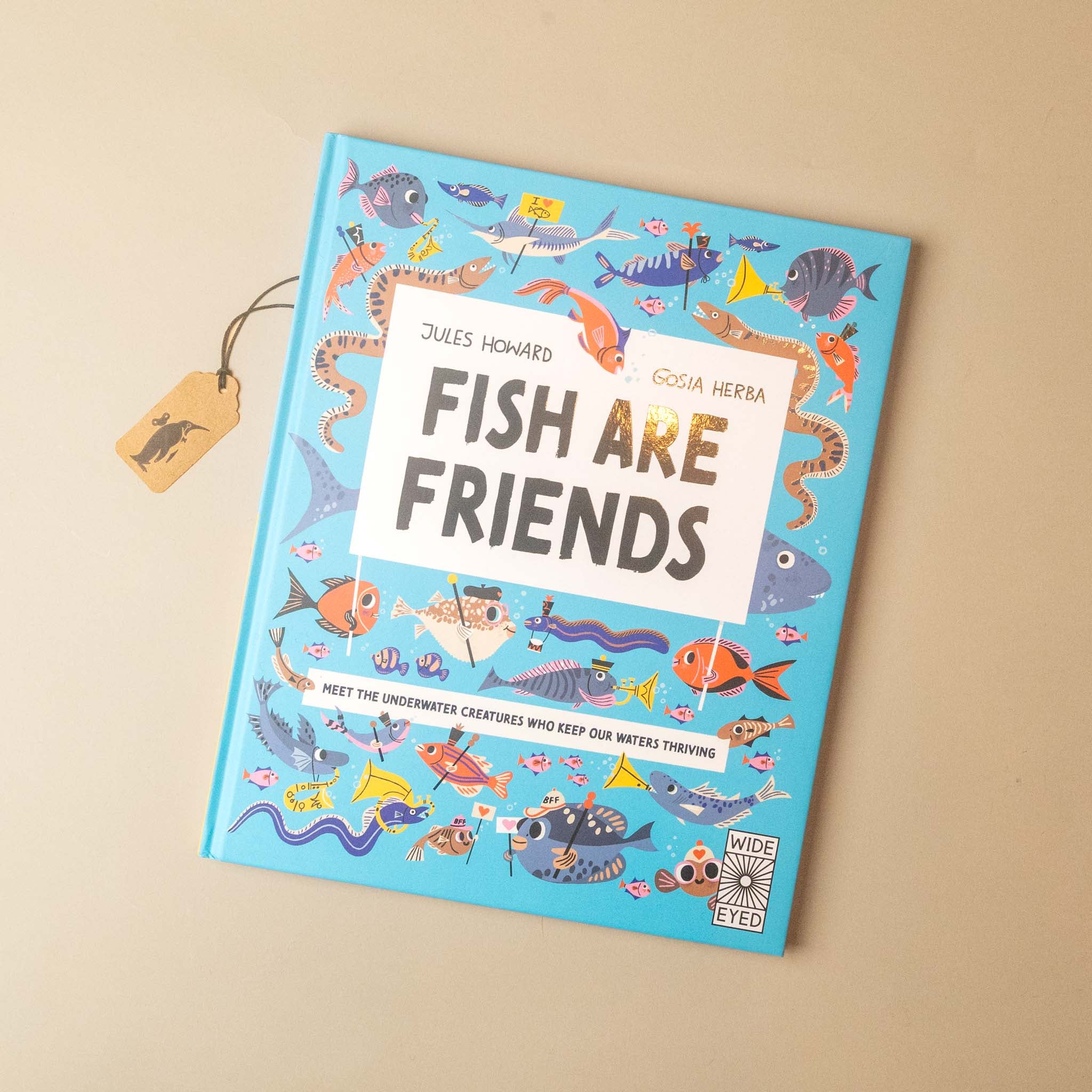 Children's book titled 'Fish Are Friends' by Jules Howard and Cosia Herria, featuring a bright blue cover illustrated with colorful fish and sea creatures, photographed on a beige background with a small paper price tag attached.