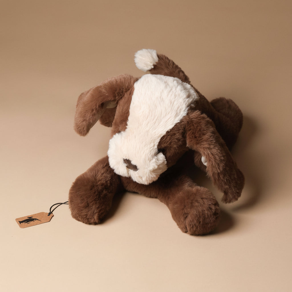 Brown plush floppy-mutt-cocoa toy with a white patch on a beige background
