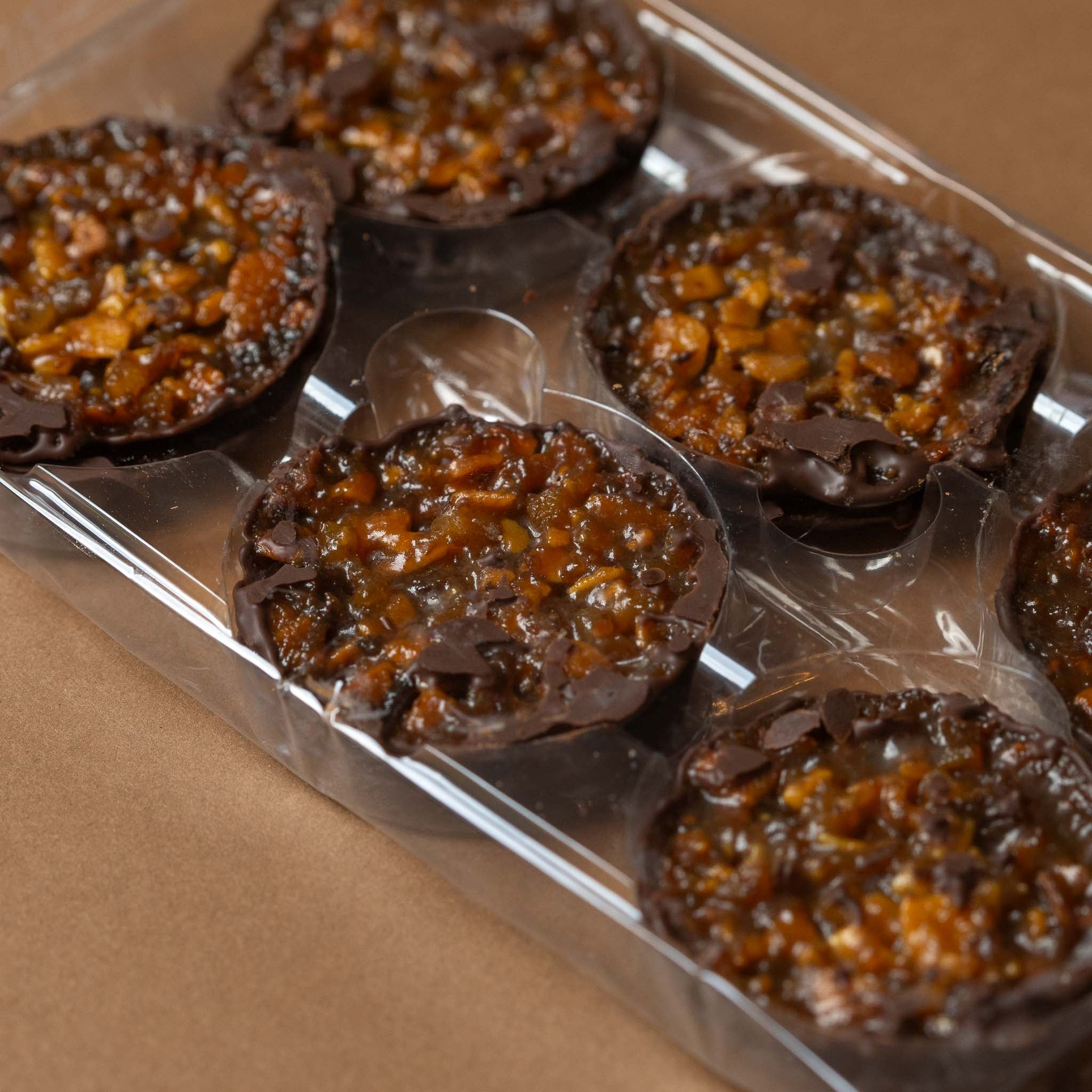 florentins-gift-box-dark-chocolate-with-orange Chocolate-covered treats in a clear plastic packaging on a brown background
