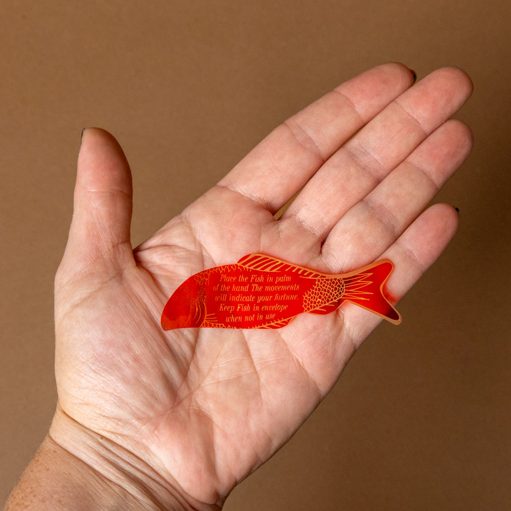fortune-fish-Hand holding a red fish-shaped object with text against a brown background