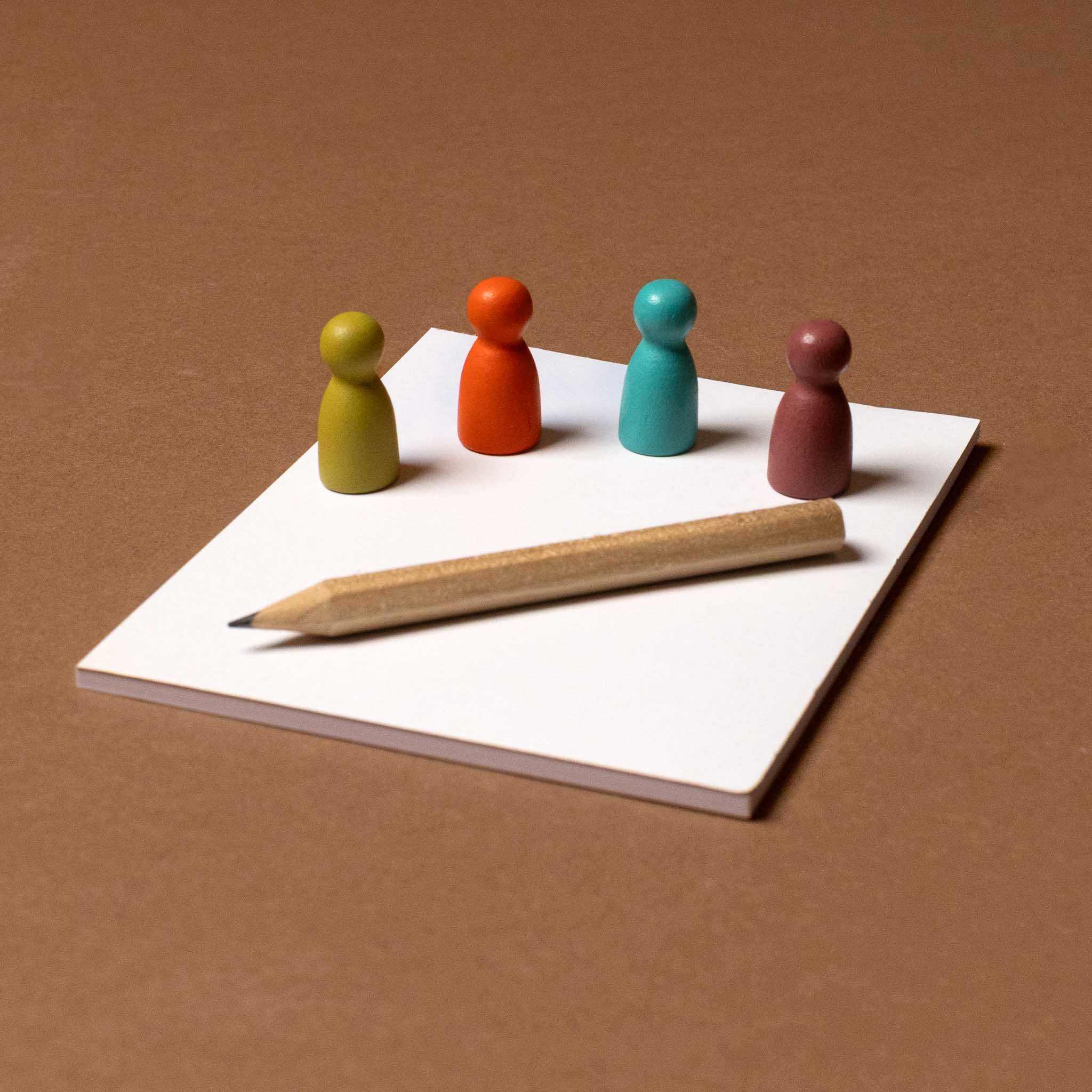 friends-and-family-games-night Colorful wooden figures and a pencil on a white sheet of paper with a brown background