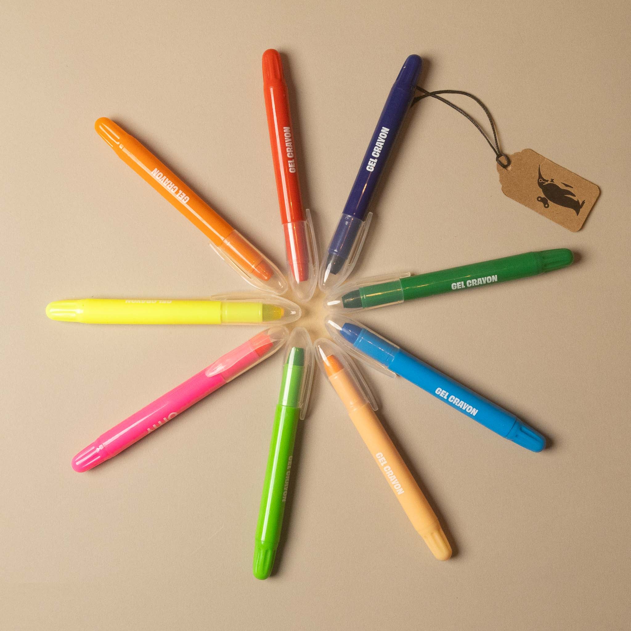 gelly-flow-gel-crayon-set-9pc  in assorted bright colors arranged in a circular pattern on a beige background, with a small hanging tag attached.