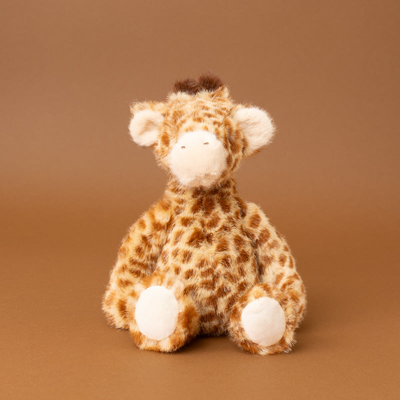 A plush stuffed giraffe toy with a brown and beige spotted pattern, sitting against a solid brown studio background.