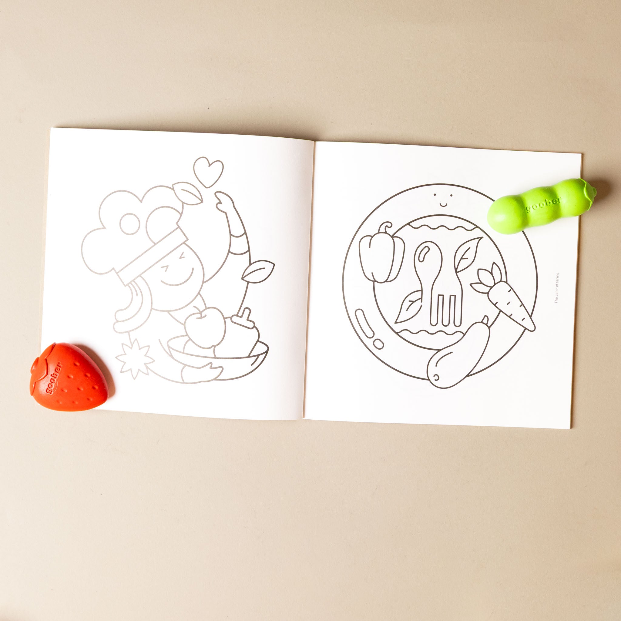 goober-farm-crayon-Open coloring book with two designs on a beige surface, accompanied by a strawberry and green peapod crayon