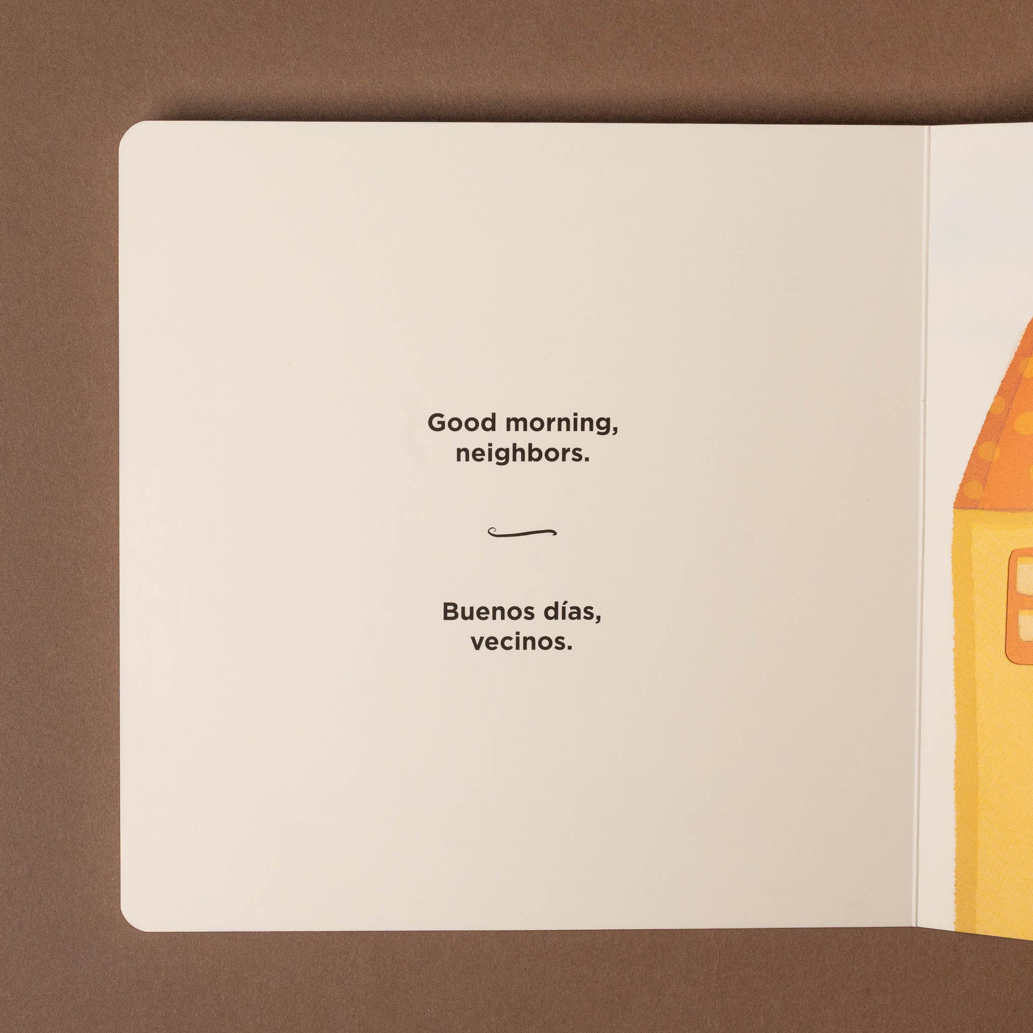 Open good-morning-buenos-dias-board-book with text 'Good morning, neighbors.' and a colorful illustration on a brown background
