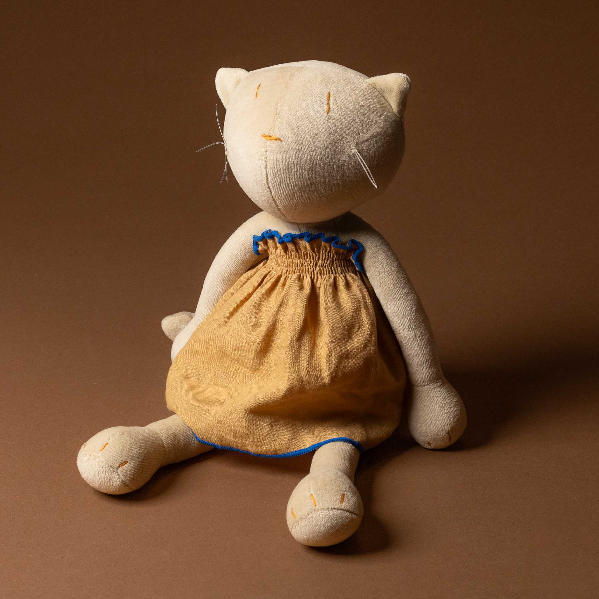 Stuffed cat toy wearing grande-outfit-linen-dress-ochre on a brown background