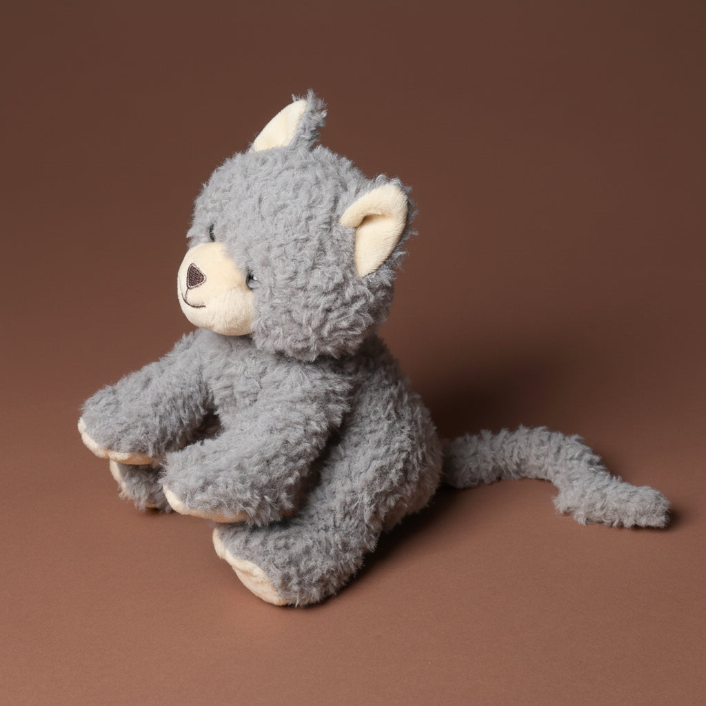 Gray plush grande-romy-the-cat--blueberry toy with a neutral expression on a brown background