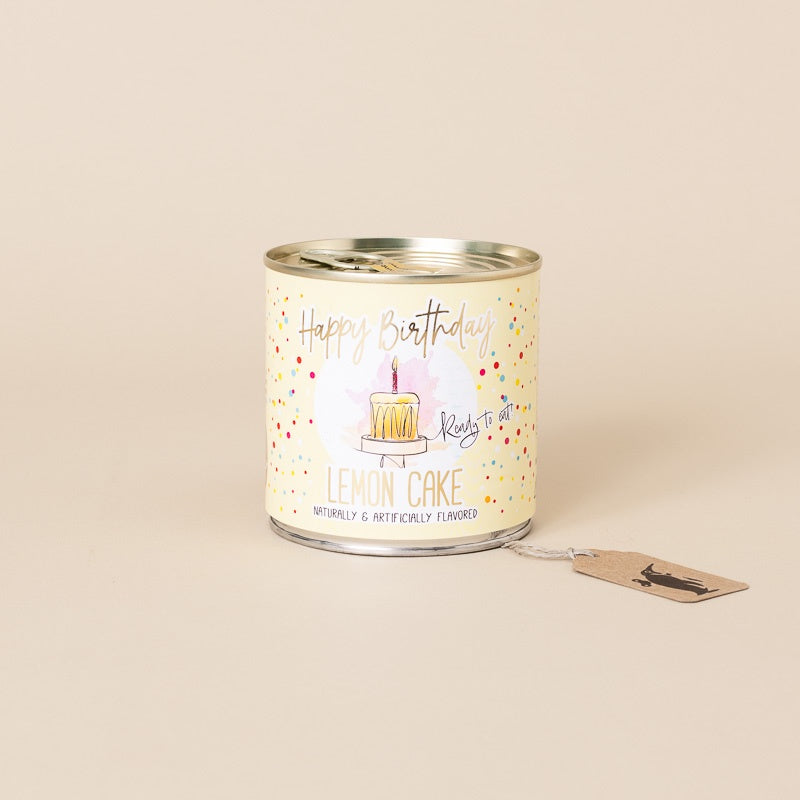 happy-birthday-cancake-lemon-cake a cream-colored label featuring a birthday cake illustration and the text 'Happy Birthday' and 'Lemon Cake,' shown on a plain beige background with a small hang tag attached.