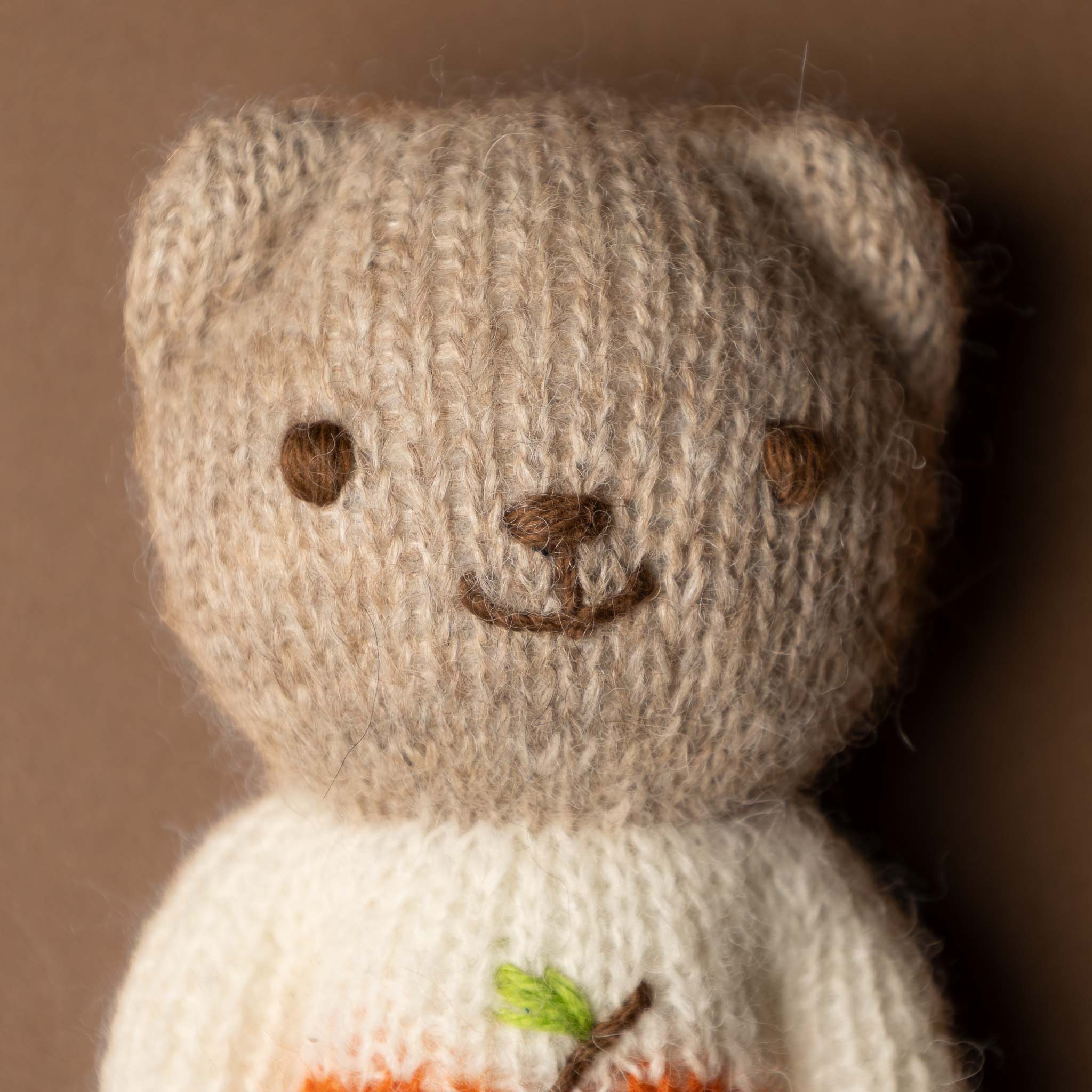 happy-go-lucky-bear Knitted teddy bear with a brown face and white body against a brown background