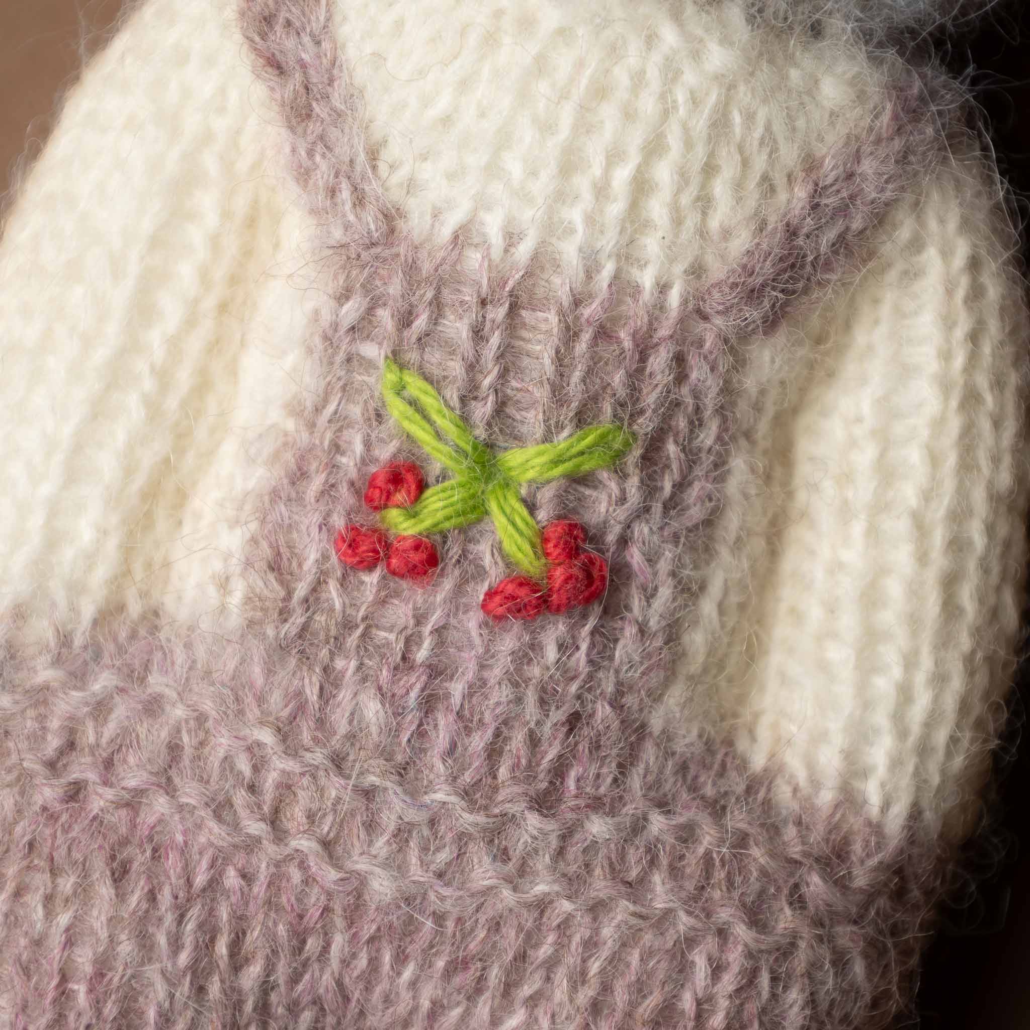 happy-go-lucky-cat Close-up of a knitted fabric with embroidered red flowers and green leaves.