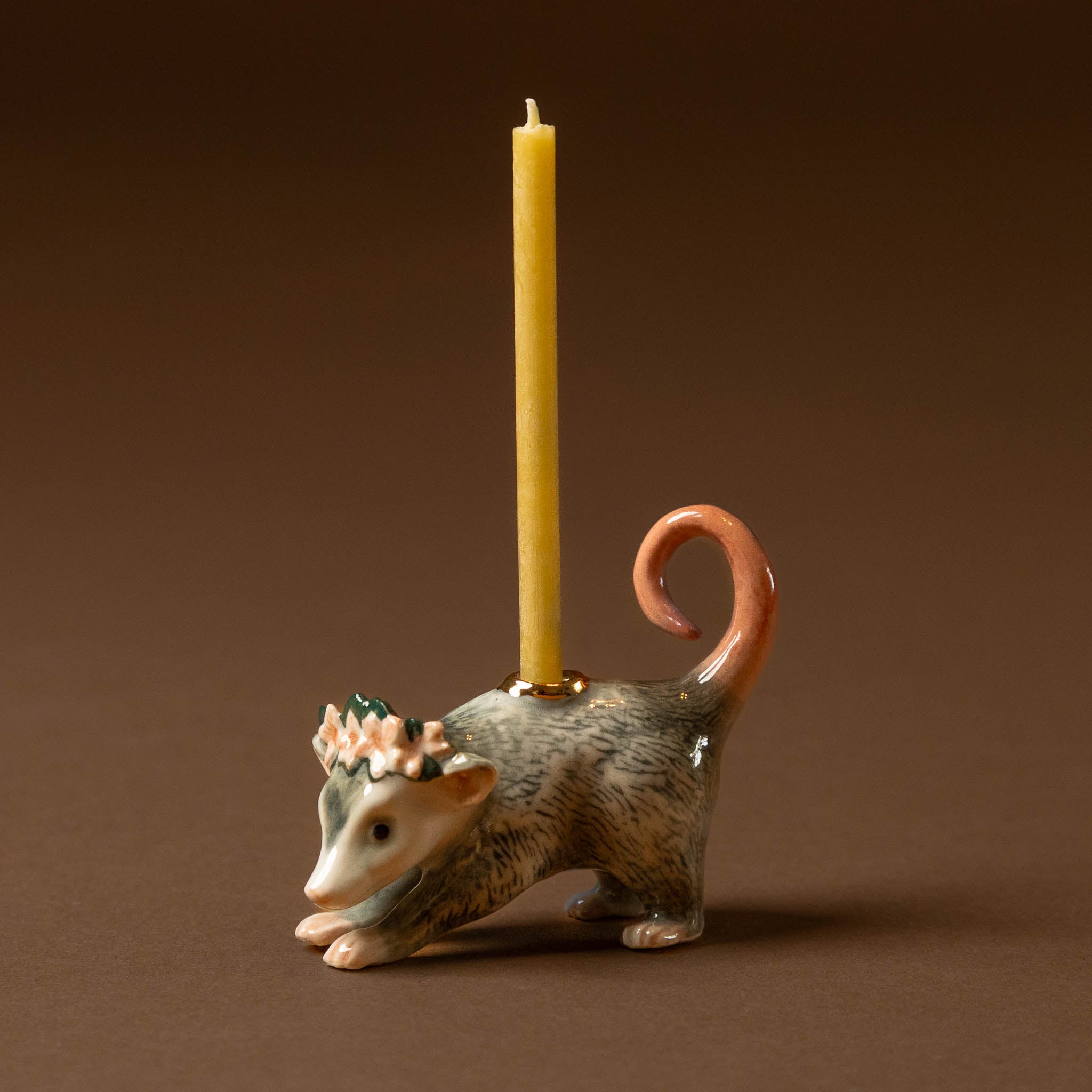 Ceramic opossum-shaped candle holder with a lit candle on a brown background