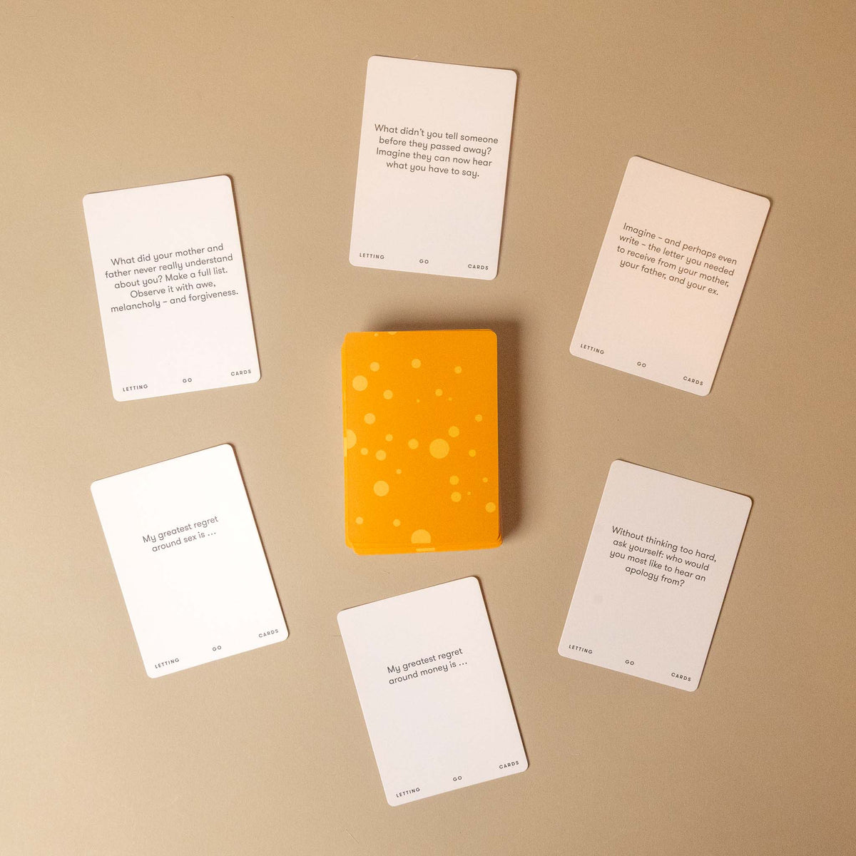 A set of white printed cards arranged around a small orange-yellow box with scattered light spots, photographed from above on a warm beige background.