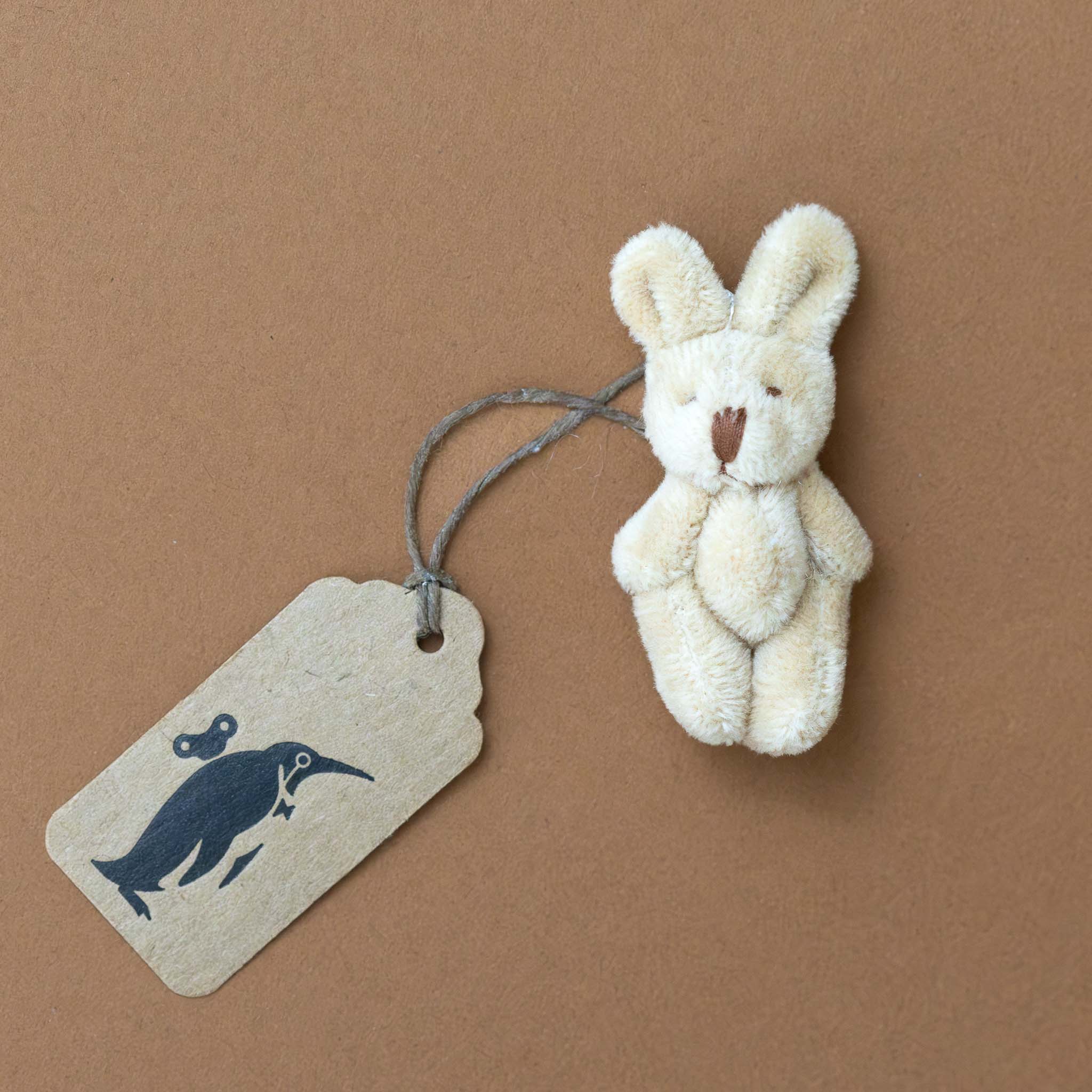 itty-bitty-bunny-oatmeal Small beige stuffed bunny with a brown paper tag featuring a black illustration on a brown background