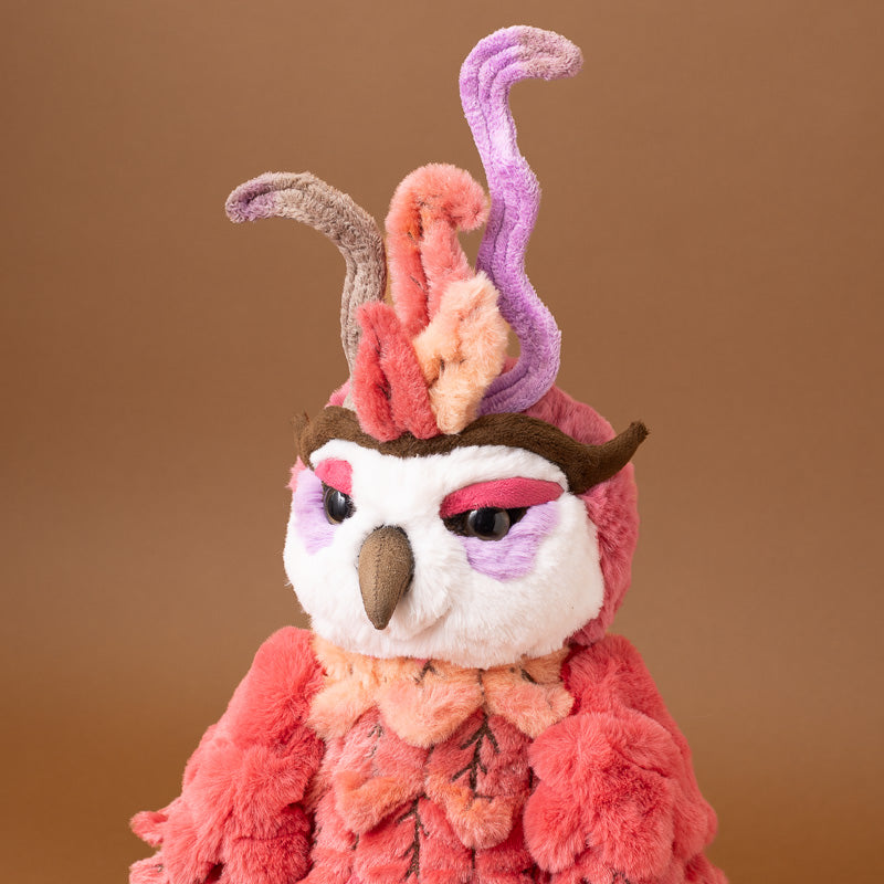 A close-up of a plush jinzi-the-rising-phoenix wearing a textured, furry costume in shades of pink, orange, purple, and brown, set against a solid warm brown background.
