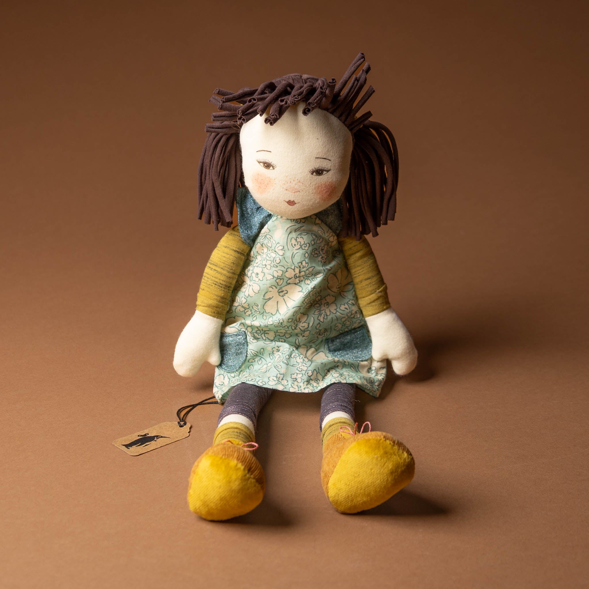 les-rosalie-rag-doll-iris Stuffed doll with brown hair and yellow shoes on a brown background