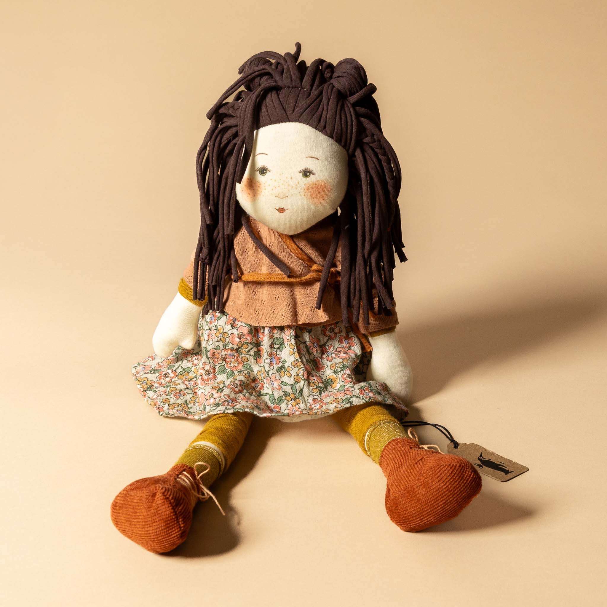 les-rosalie-rag-doll-marjolaine Stuffed doll with brown hair and floral dress on a beige background