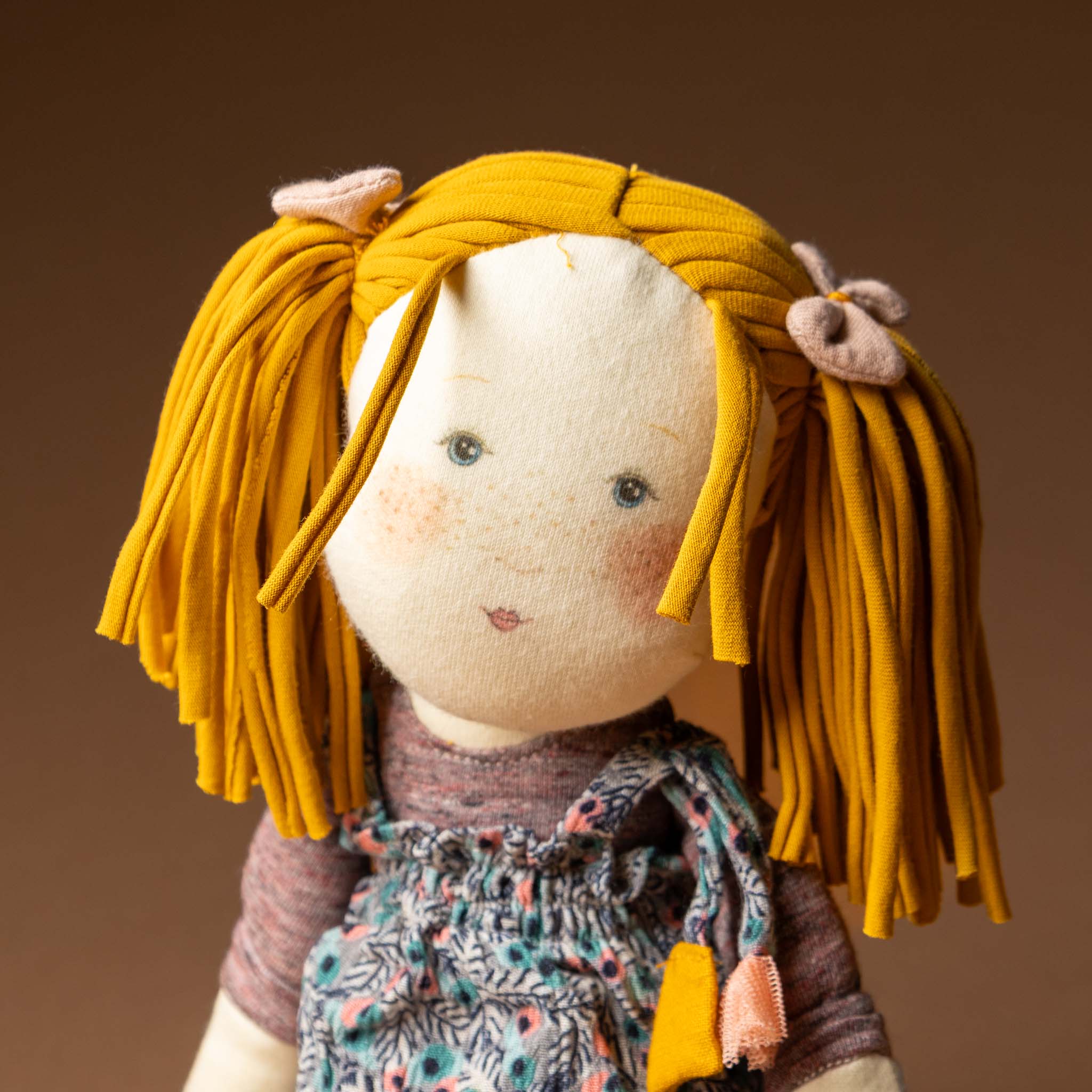 les-rosalies-rag-doll-violette Stuffed toy with yellow hair and a patterned dress on a brown background