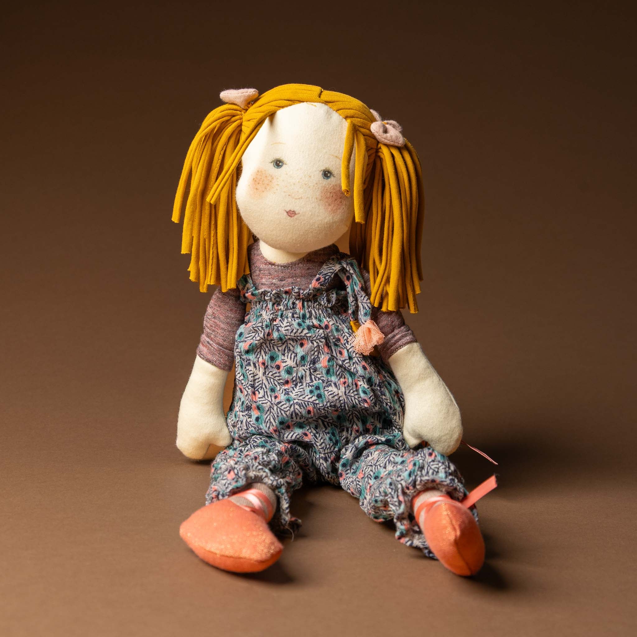 les-rosalies-rag-doll-violette Stuffed toy with yellow hair and floral dress on a brown background