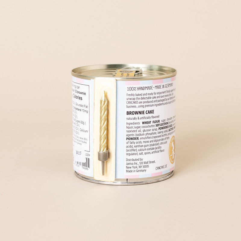 A single can of handcrafted brownie cake cookies on a solid beige background, showing the back of the label with product details and a small gold ribbon tied to the can.
