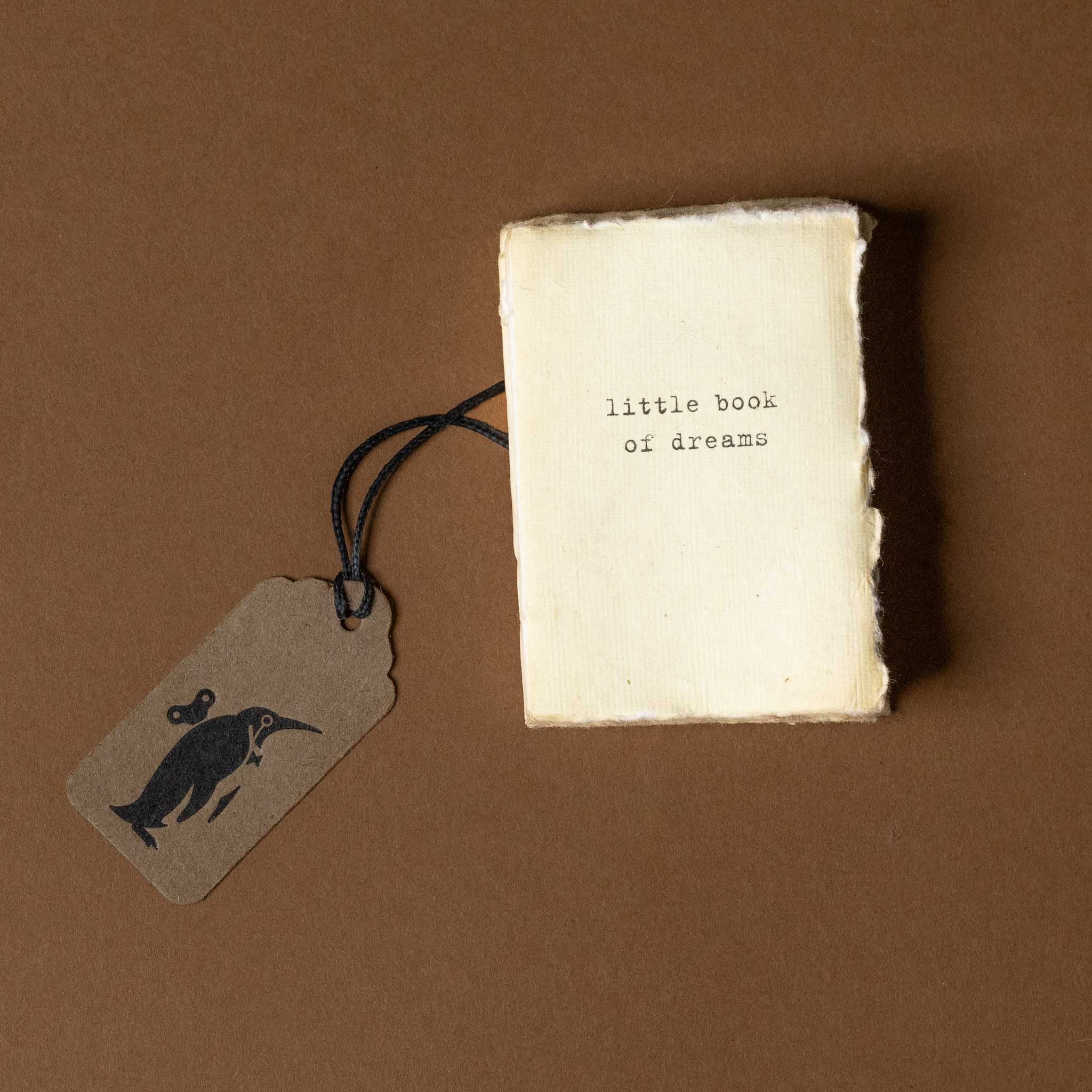 Small book titled 'little book of dreams' with a tag featuring a dolphin illustration on a brown background
