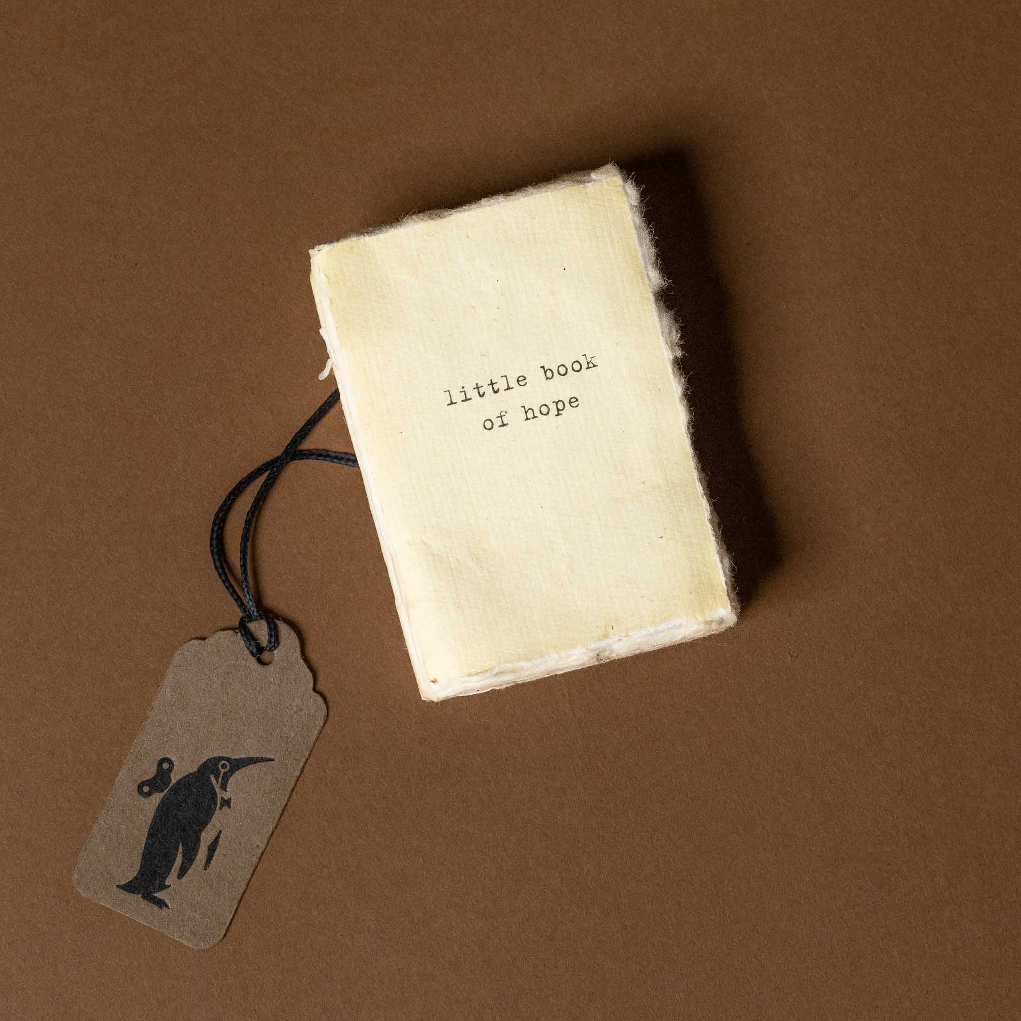 Small book titled 'little book of hope' with a tag featuring a penguin illustration on a brown background