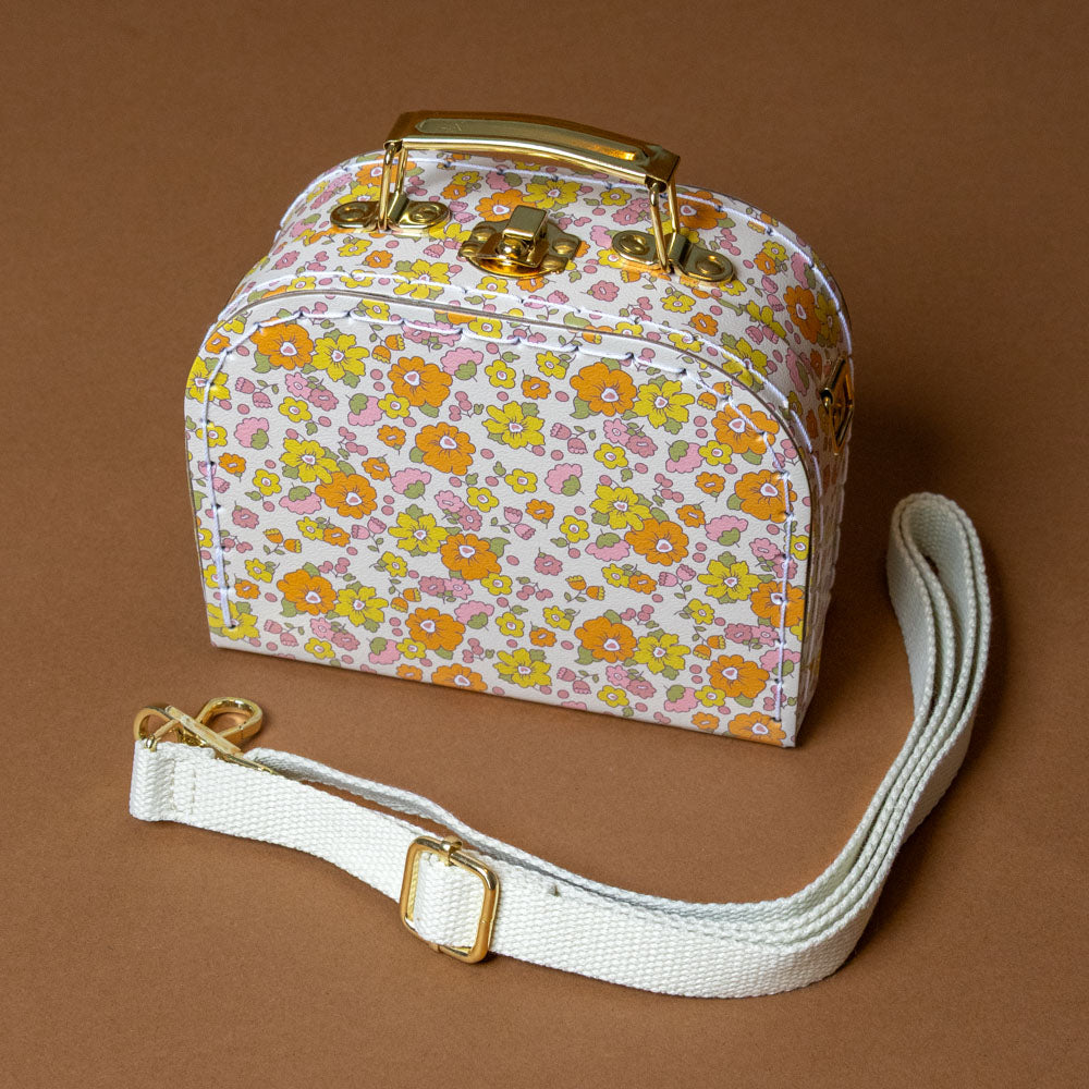 little-cross-body-case-sweet-marigold Floral-patterned suitcase with a white strap on a brown background