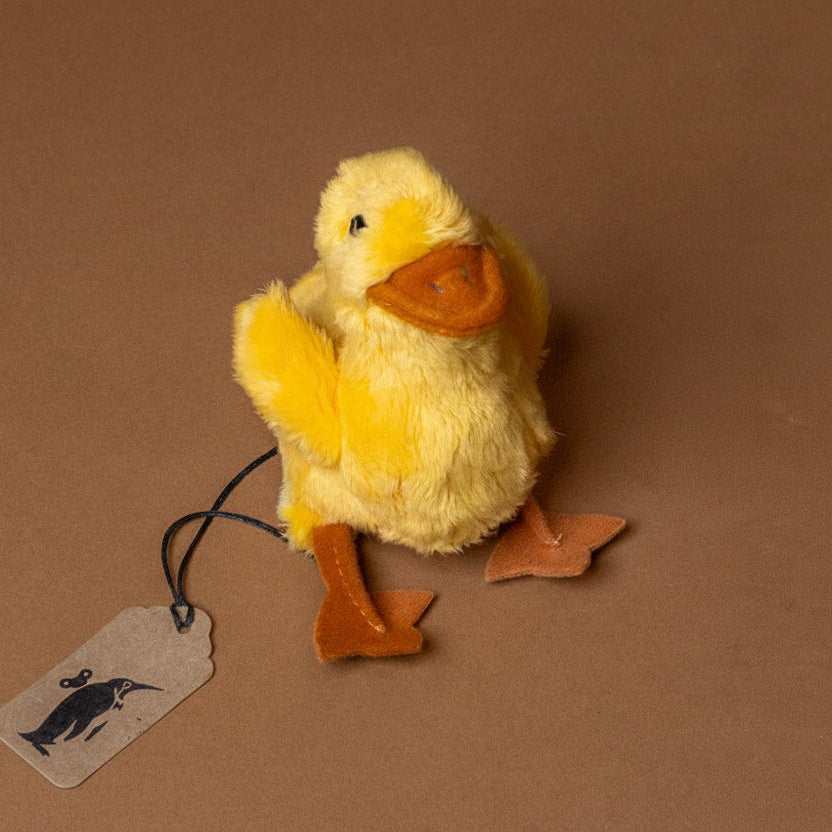 little-duck-chick-finger-puppet Yellow plush duck with a tag on a brown background