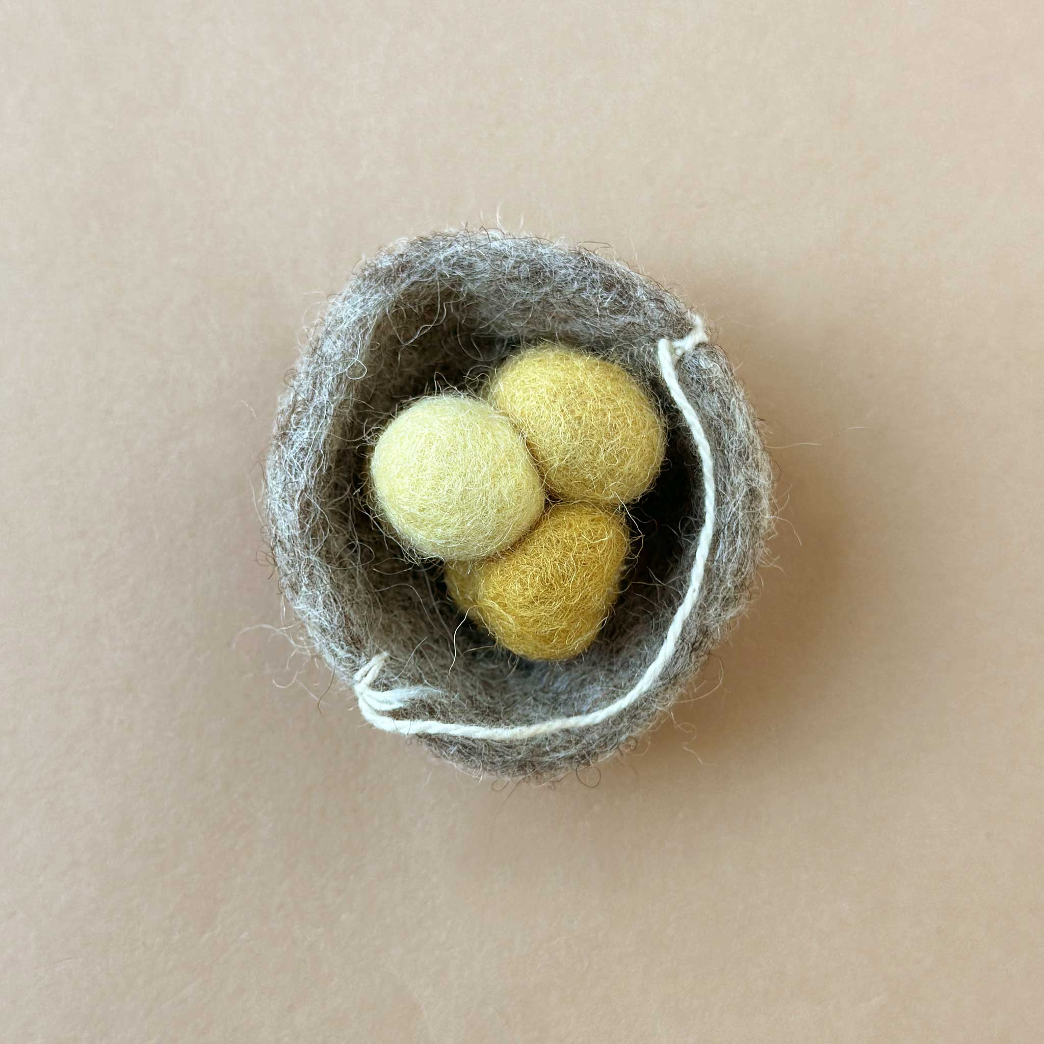 grey felted nest from above with three yellow eggs