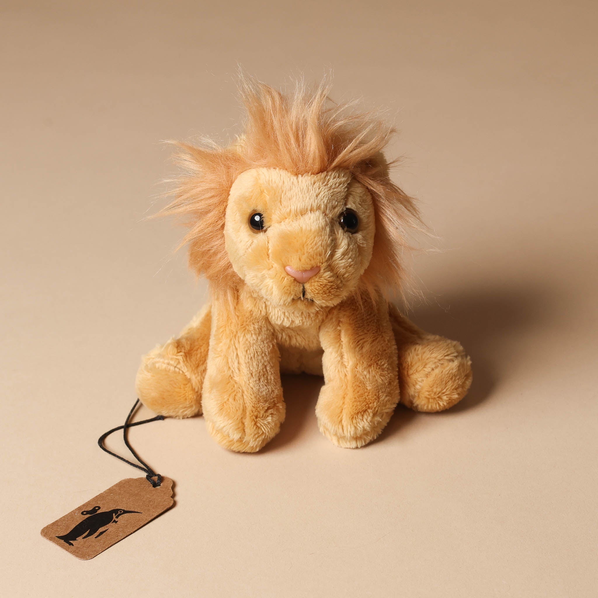 Plush little-lion-cub toy with a tag on a beige background