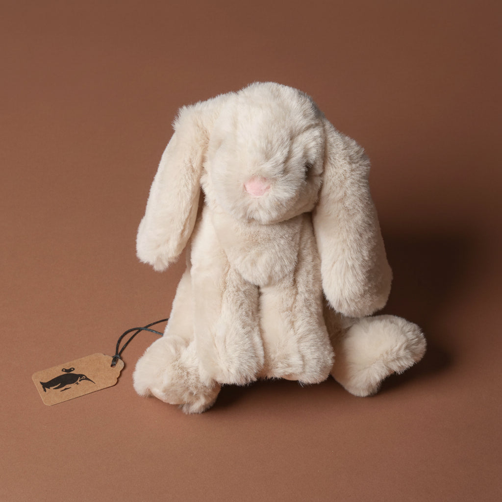 Plush little-lottie-bunny-beige toy with a tag on a brown background