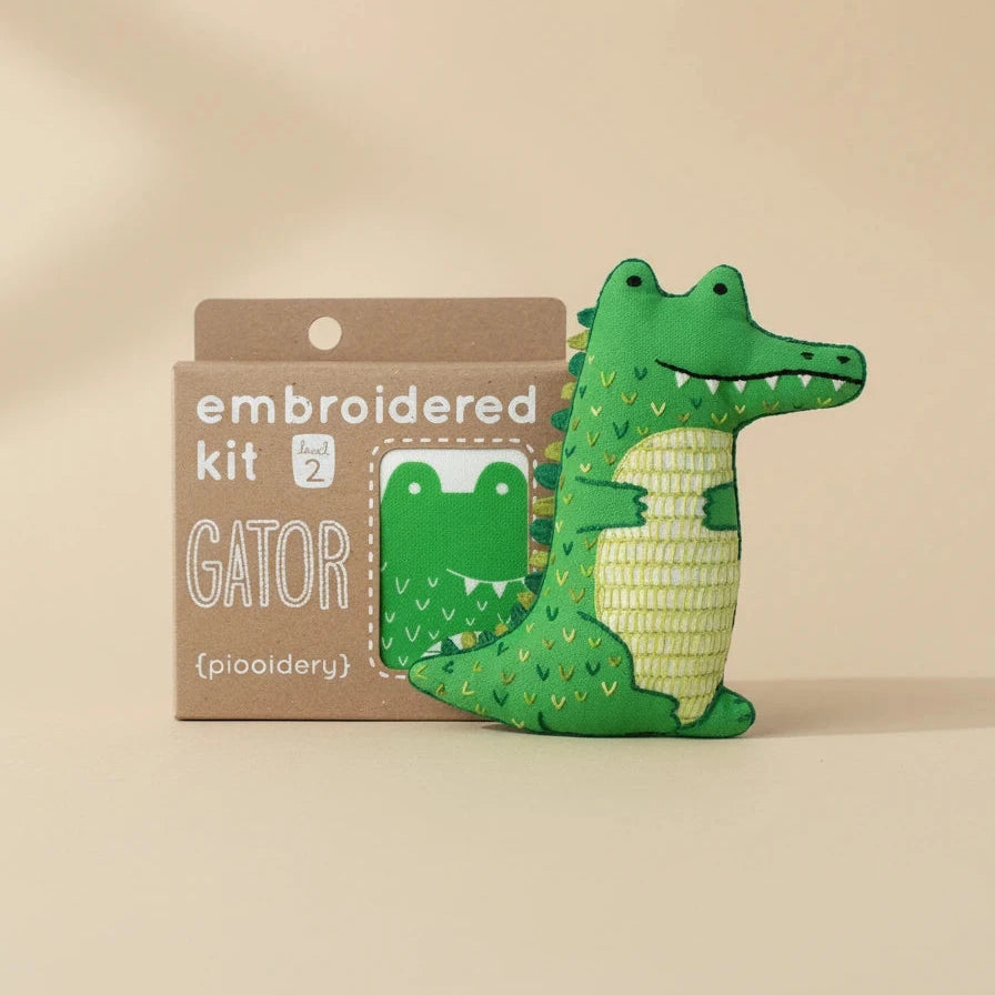 Green alligator embroidered doll kit with brown packaging on a white background