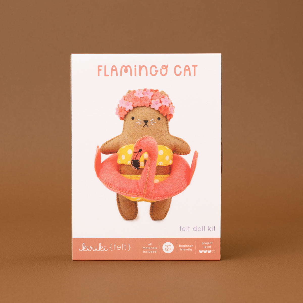 The product packaging box for the 'Flamingo Cat' felt doll kit (felt), featuring a white box with a colorful illustration of a brown cat wearing a pink flower crown and yellow polka-dot float, set against a solid brown background.