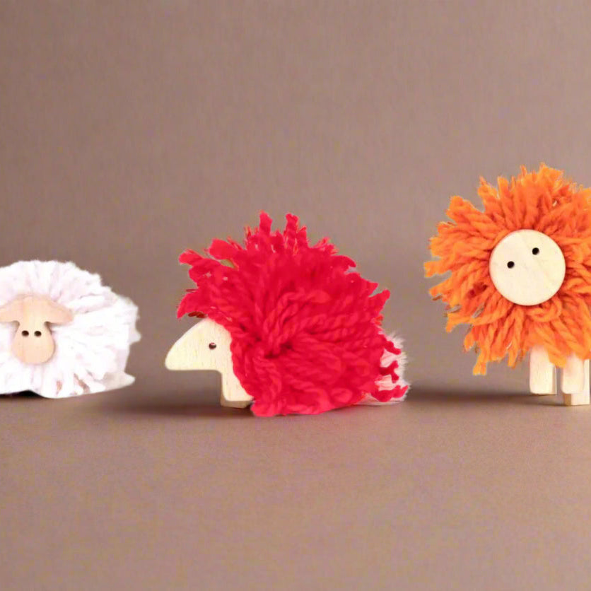 Three colorful make-your-own-pom-pom-animal toys on a brown background
