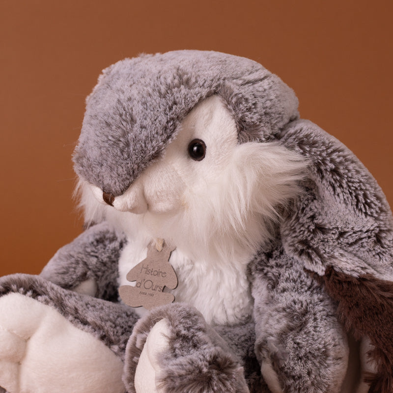 A plush stuffed bunny,seated against a solid warm brown studio background. The toy has soft gray and white fur, dark brown inner ears
