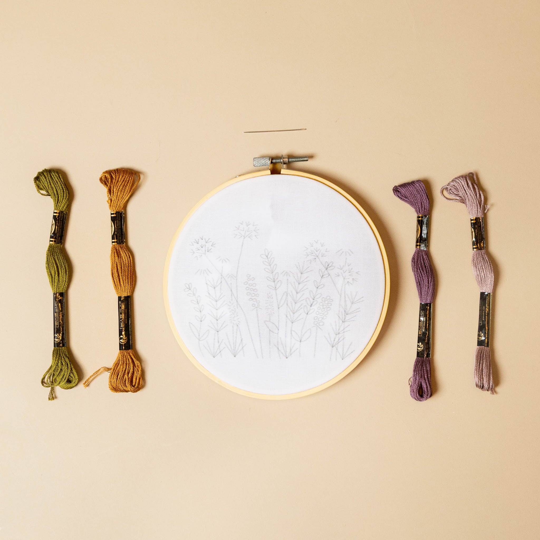 meadow-embroidery-kit-plum Embroidery hoop with white fabric and four skeins of embroidery thread on a beige background