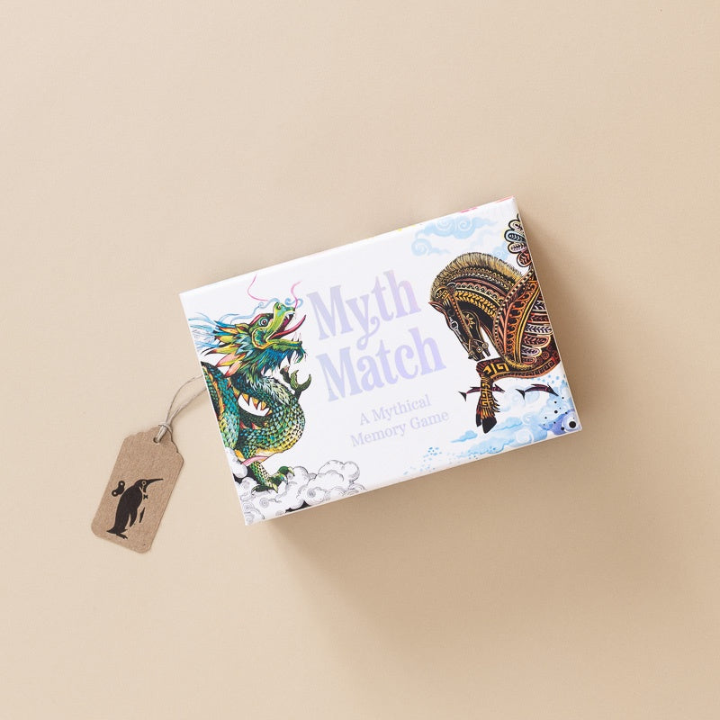A boxed card game called 'Myth Match' lies on a warm beige background. The box is white with illustrated artwork of a green dragon and a golden airship, plus the text 'Myth Match' and 'A Mythical Memory Game.