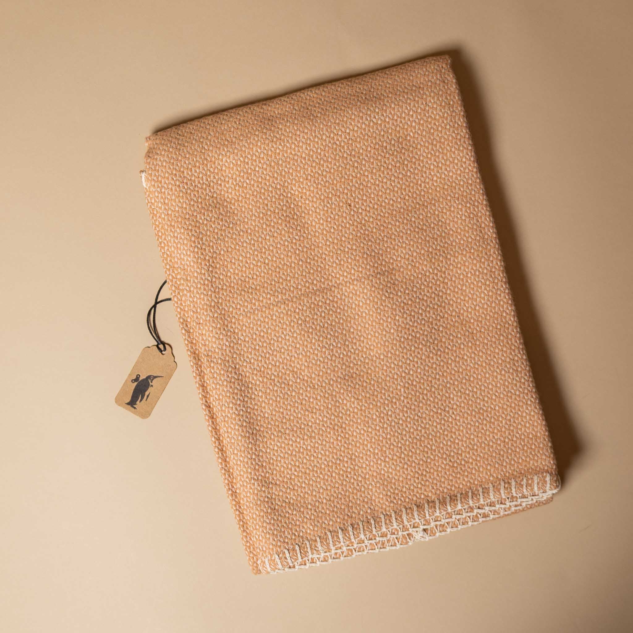 organic-cotton-stitch-blanket-blush Beige woven fabric with a tag on a beige background