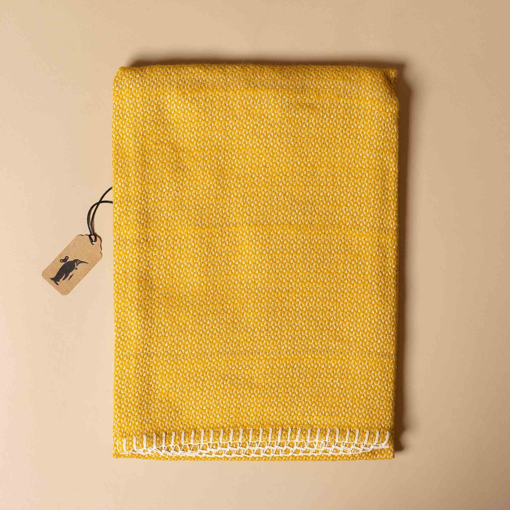 organic-cotton-stitch-blanket-ochre Yellow textured fabric with a white border on a beige background