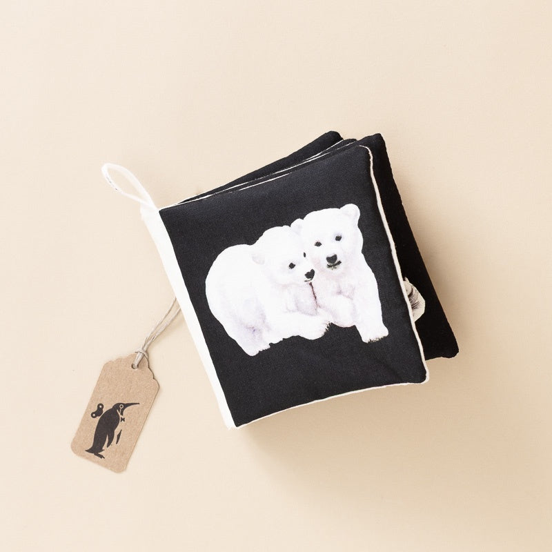 A black fabric book with a white polar bear illustration on the front, shown on a warm beige background with a small paper tag attached.