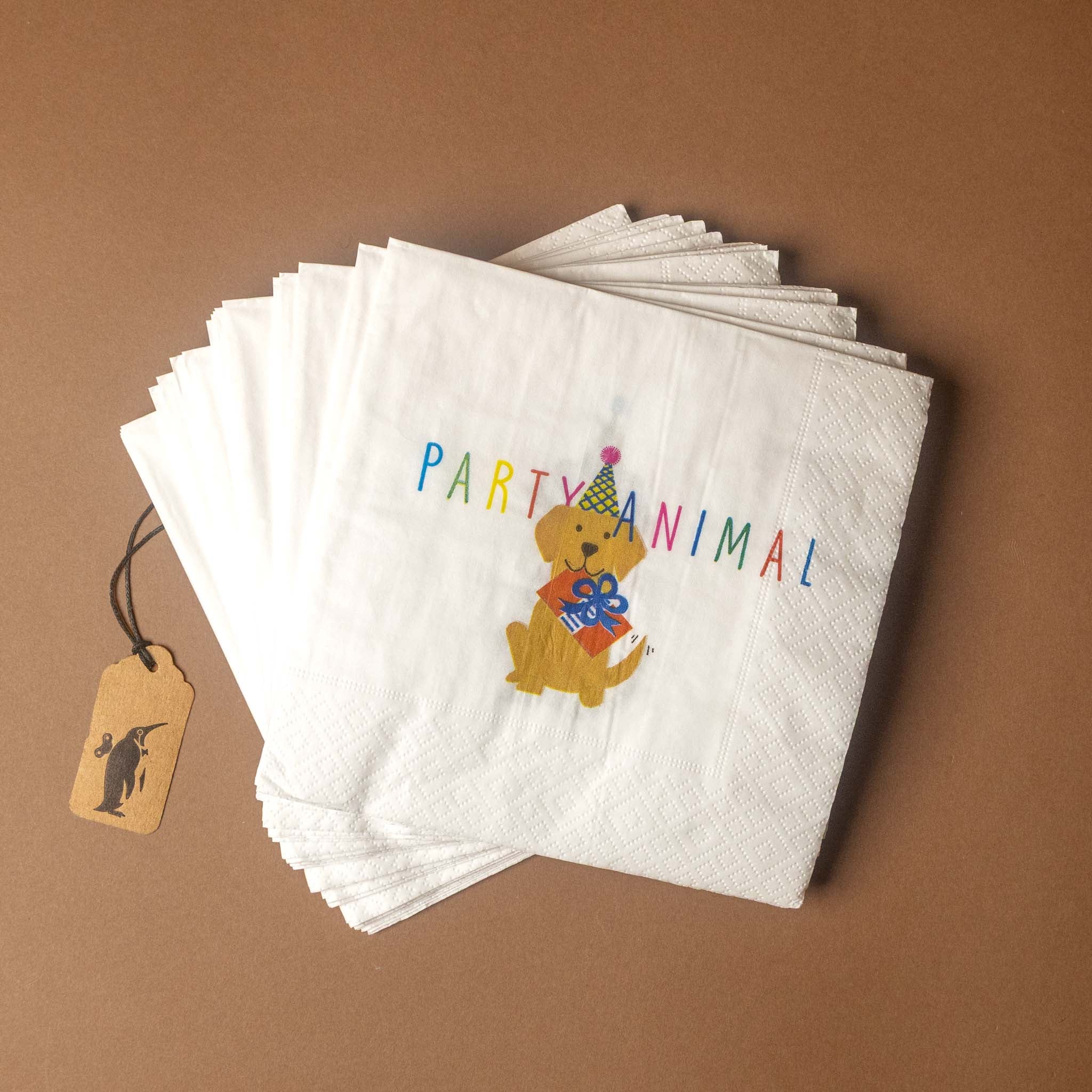 A stack of white paper napkins with a colorful 'PARTY ANIMAL' design featuring a cartoon dog holding a gift, displayed on a brown background with a small paper tag.