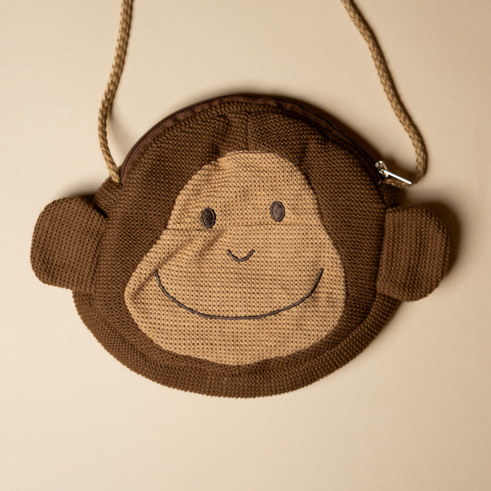 paulo-the-monkey-pocket-purse Brown monkey-shaped pouch with a smiley face on a beige background