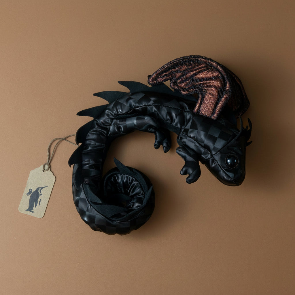 petite-dragon-wristlet-midnight Black dragon figurine with a brown tag on a beige background