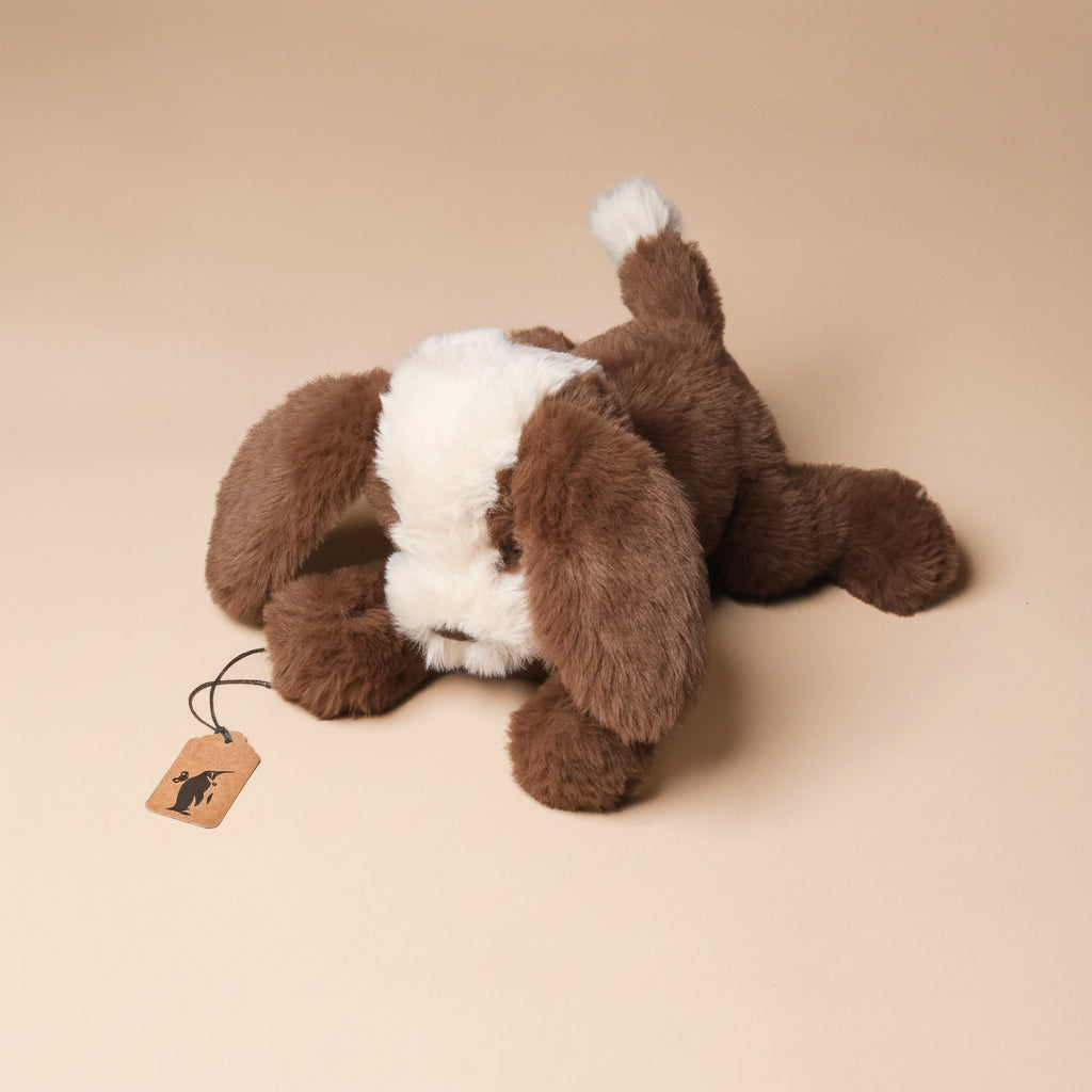 Plush petite-floppy-mutt-cocoa toy with a tag on a beige background