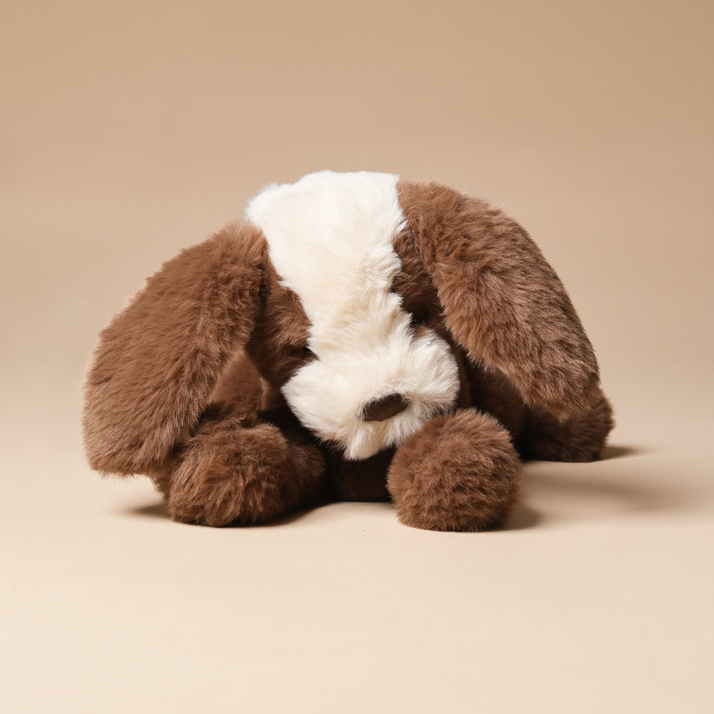 Plush toy resembling a petite-floppy-mutt-cocoa with brown fur and white face on a beige background