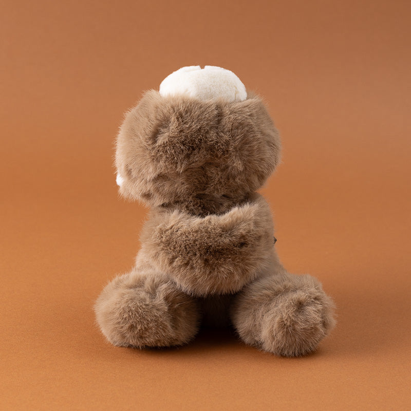 A small plush petite-gluepot-bear in brown faux fur with a white snout and ears, sitting on a solid warm brown background