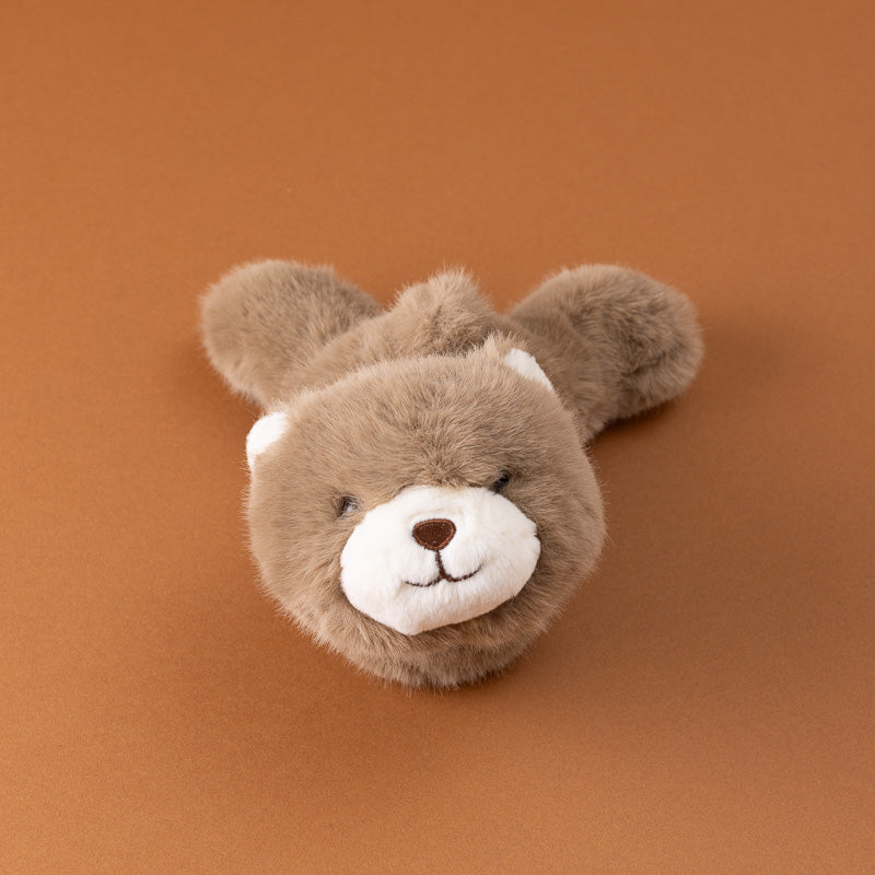 A small plush petite-gluepot-bear in brown faux fur with a white snout and ears, sitting on a solid warm brown background