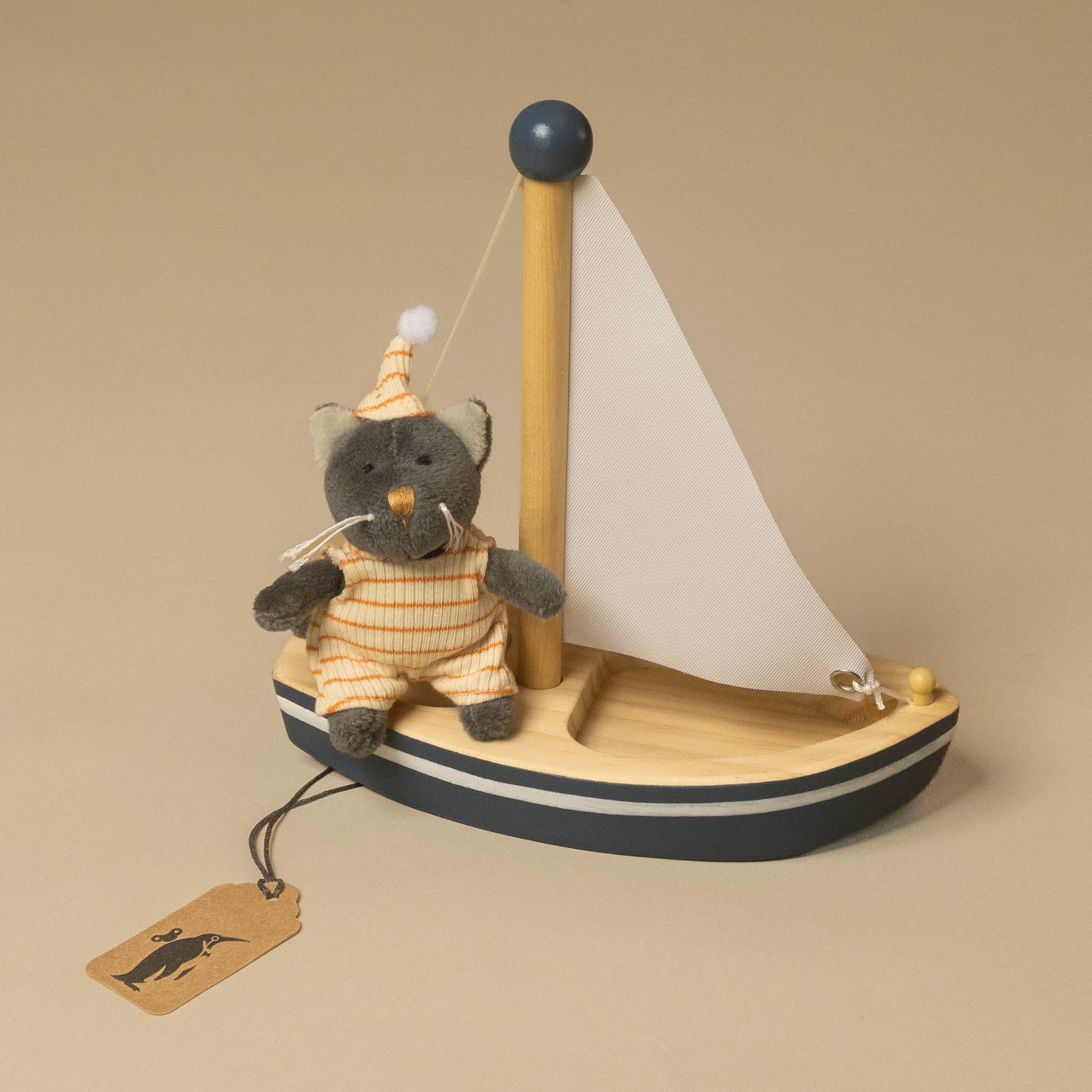 A small plush petits-amis-sail-a-way-boat-malo-cat gainst a plain beige background. The cat is gray and wears an orange-and-white striped outfit and matching hat.